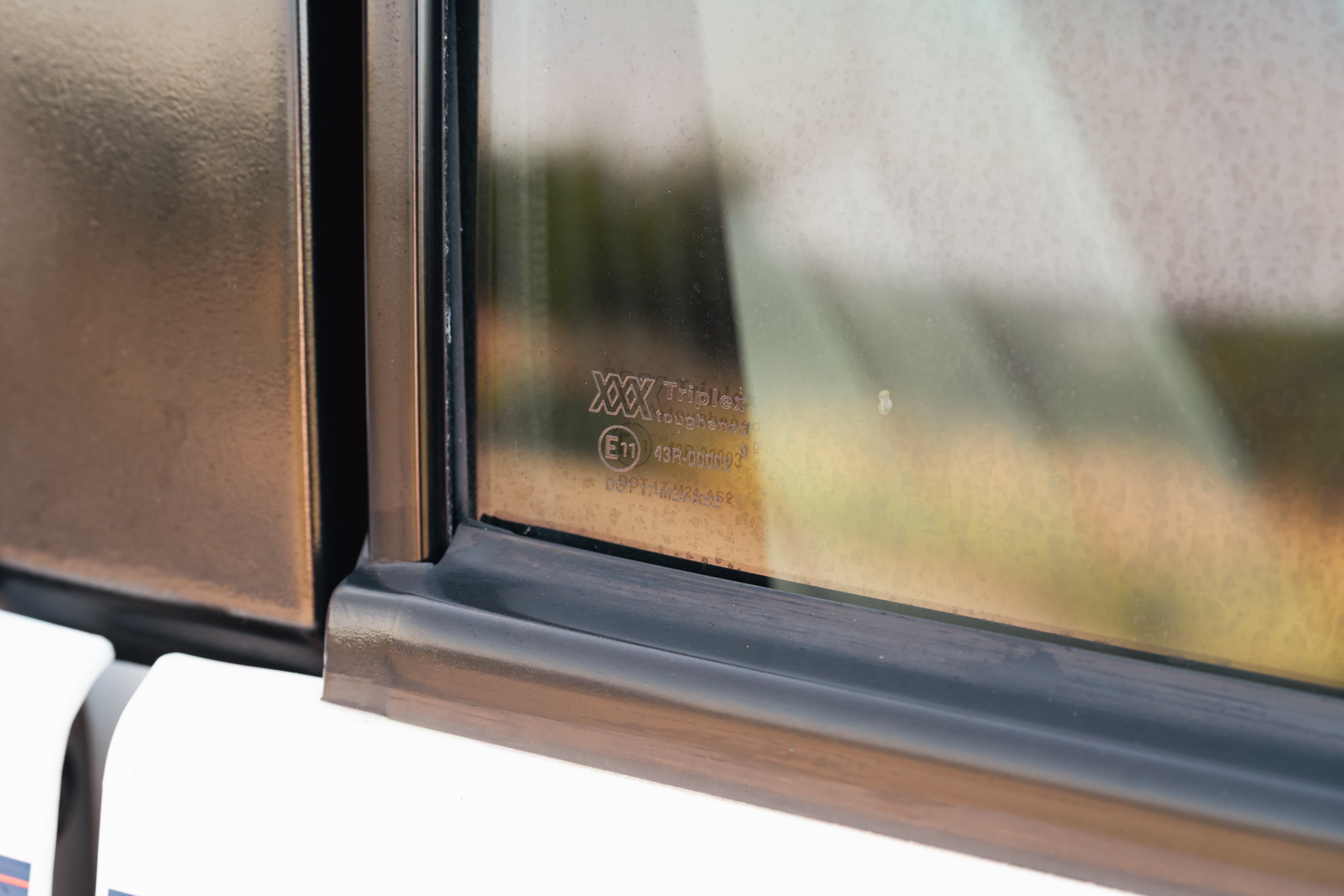 Close-up of a 1995 Range Rover County's bronze metallic body trim and tinted window with manufacturer markings.