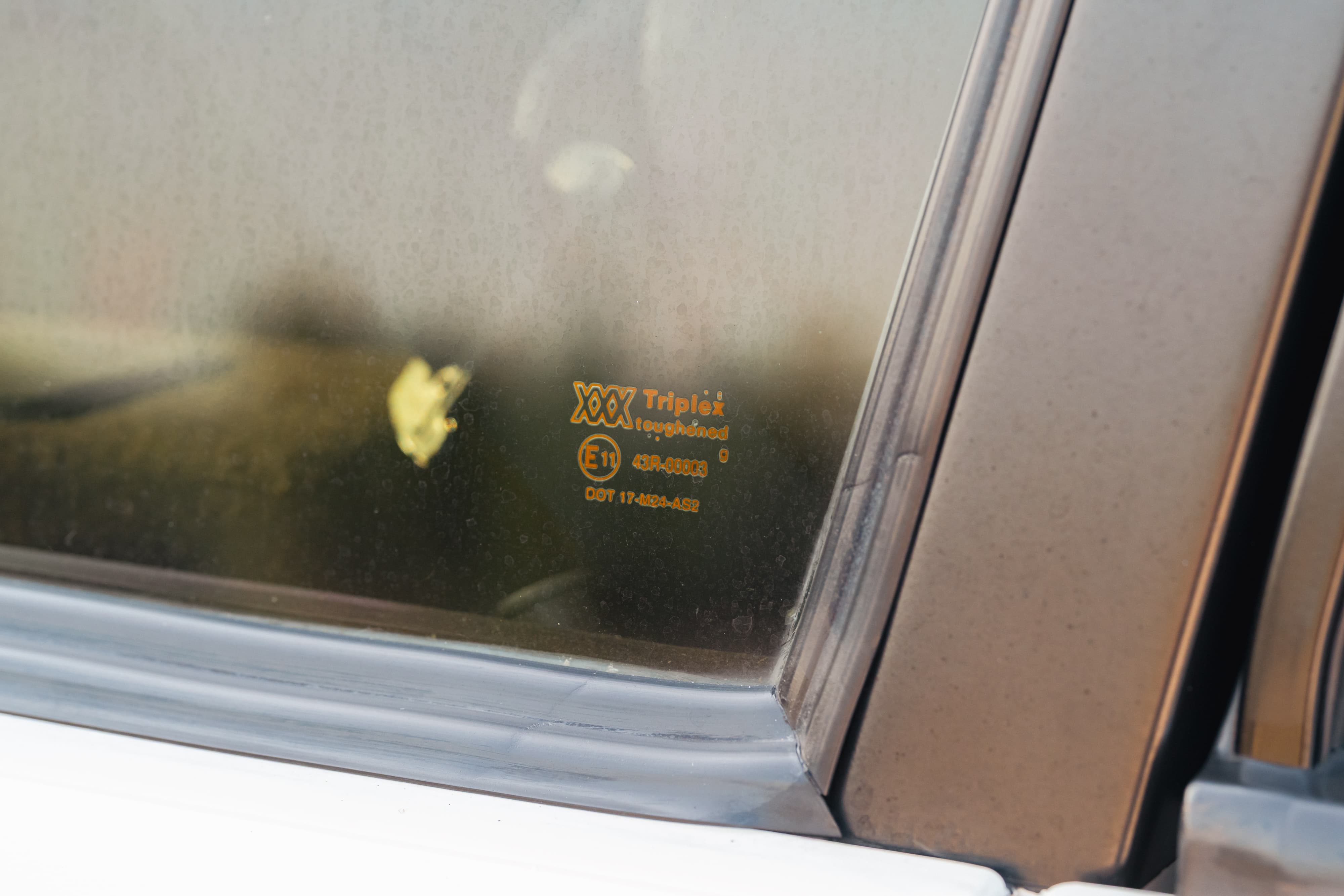 Closeup of a white 1995 Land Rover Range Rover County's side window with Triplex glass markings.