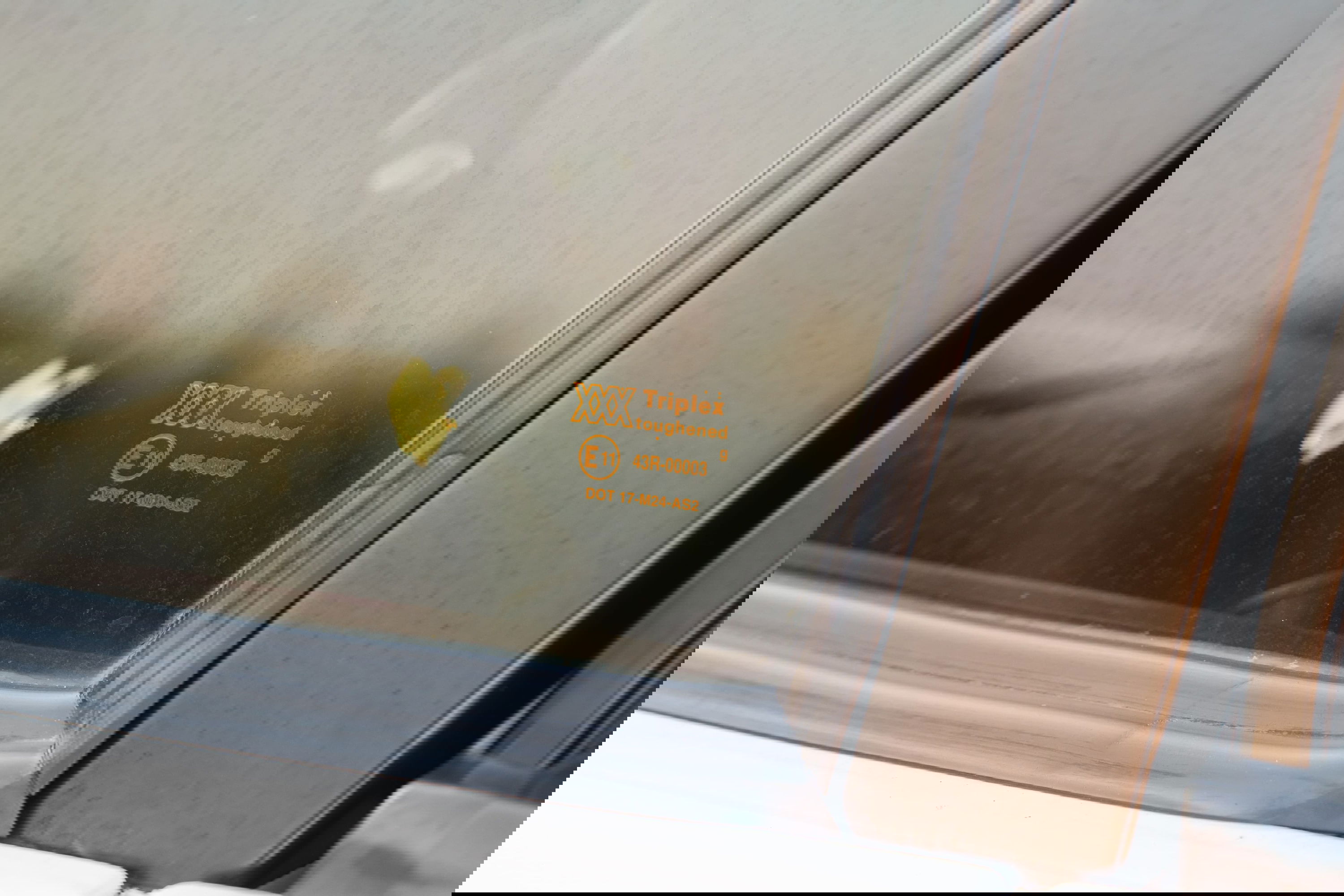 Closeup of a white 1995 Land Rover Range Rover County's side window with Triplex glass markings.