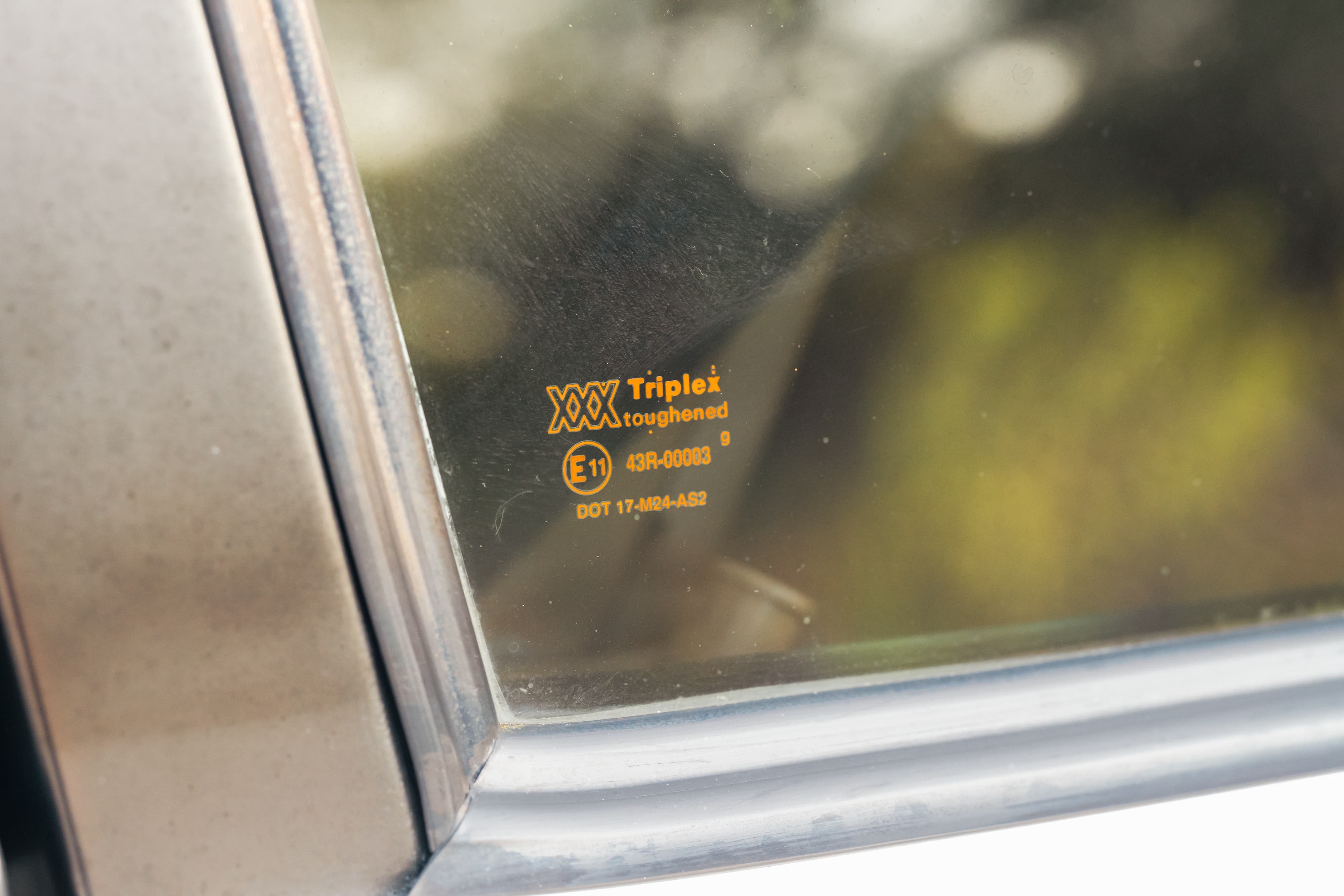 Close-up of a 1995 Land Rover Range Rover's toughened glass with Triplex markings and E11 certification.