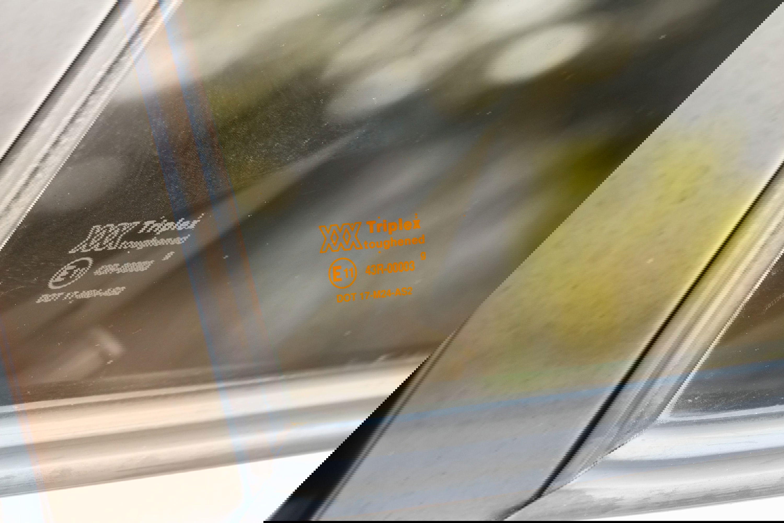 Close-up of a 1995 Land Rover Range Rover's toughened glass with Triplex markings and E11 certification.