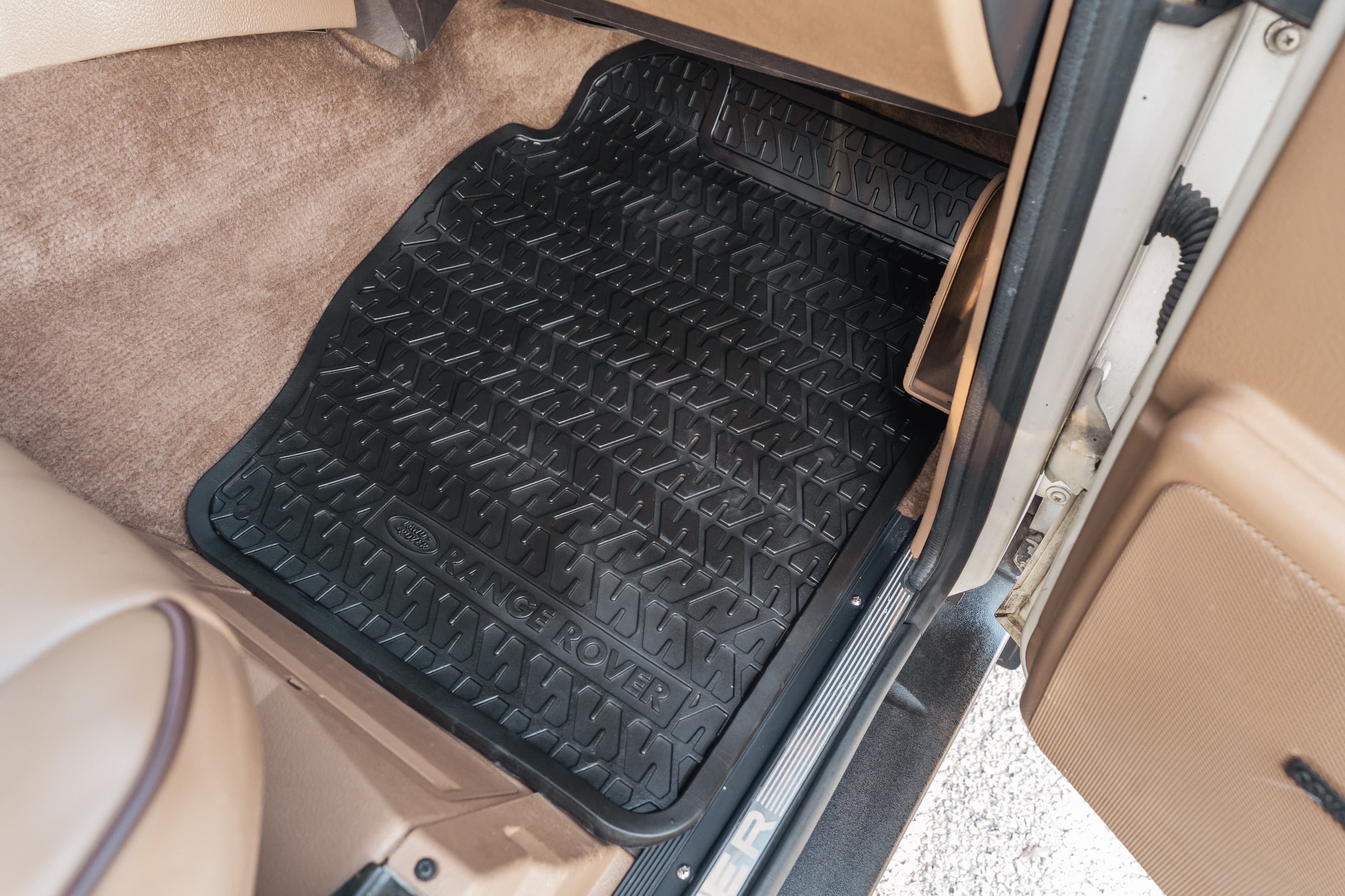Black Range Rover floor mat with &quot;RANGE ROVER&quot; text and diamond tread pattern on tan carpet.