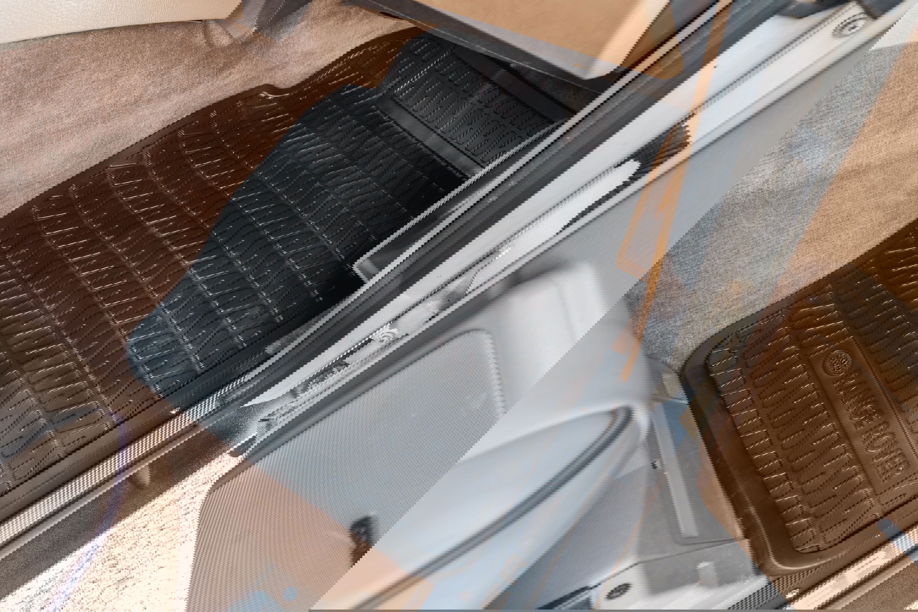 Black Range Rover floor mat with &quot;RANGE ROVER&quot; text and diamond tread pattern on tan carpet.