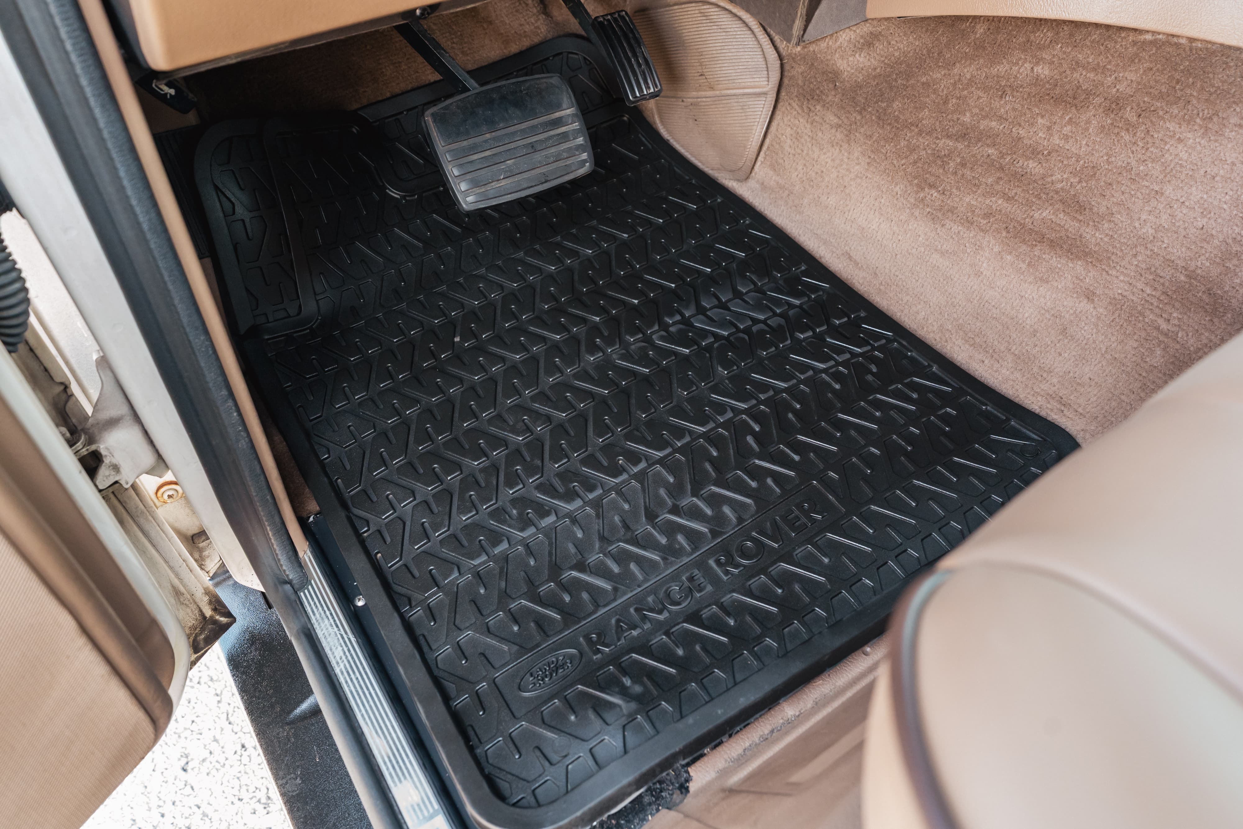 Black Range Rover floor mats with a tire tread pattern on beige carpet.