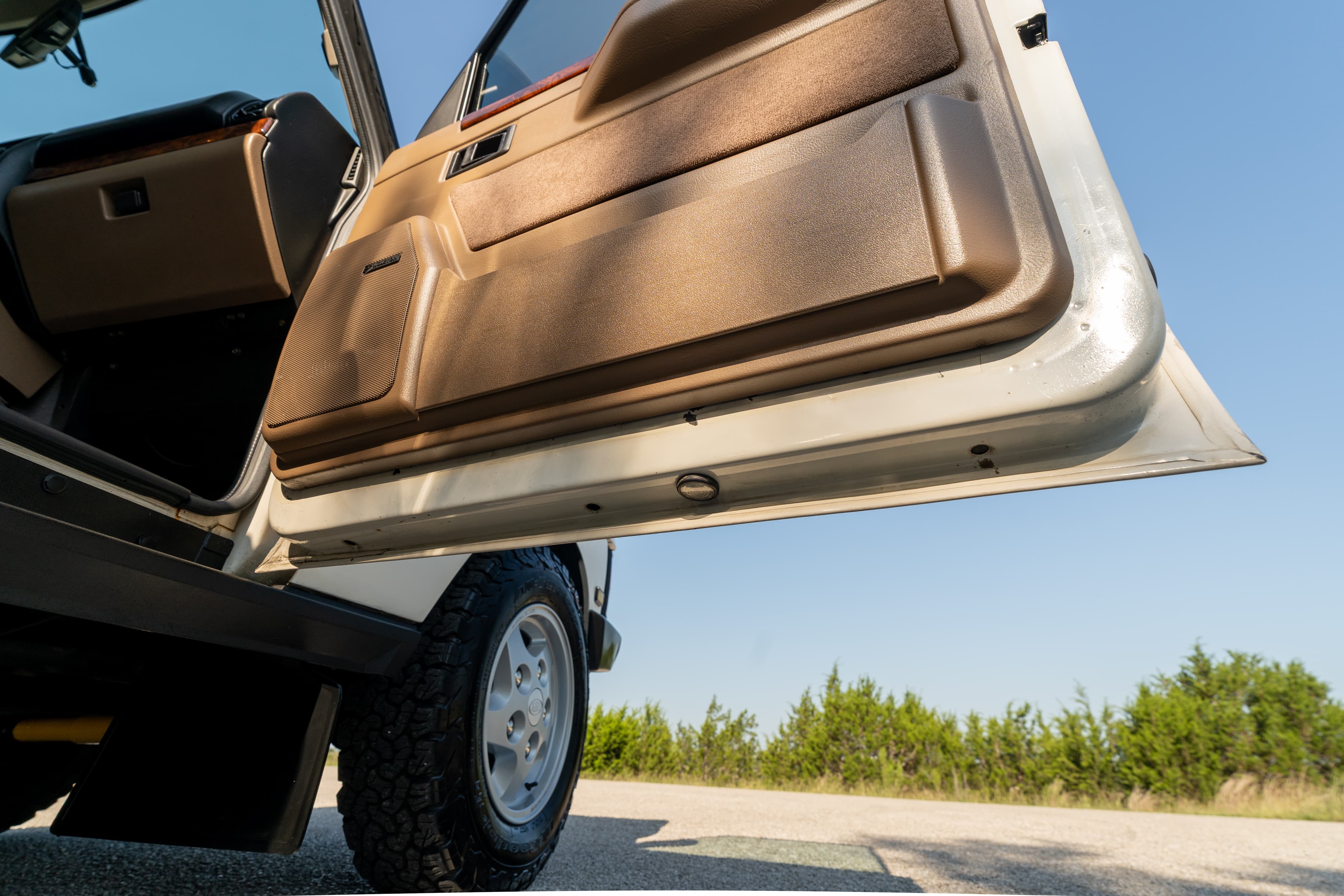 1995 Range Rover County door open, showing tan trim, and off-road tire with classic rims.