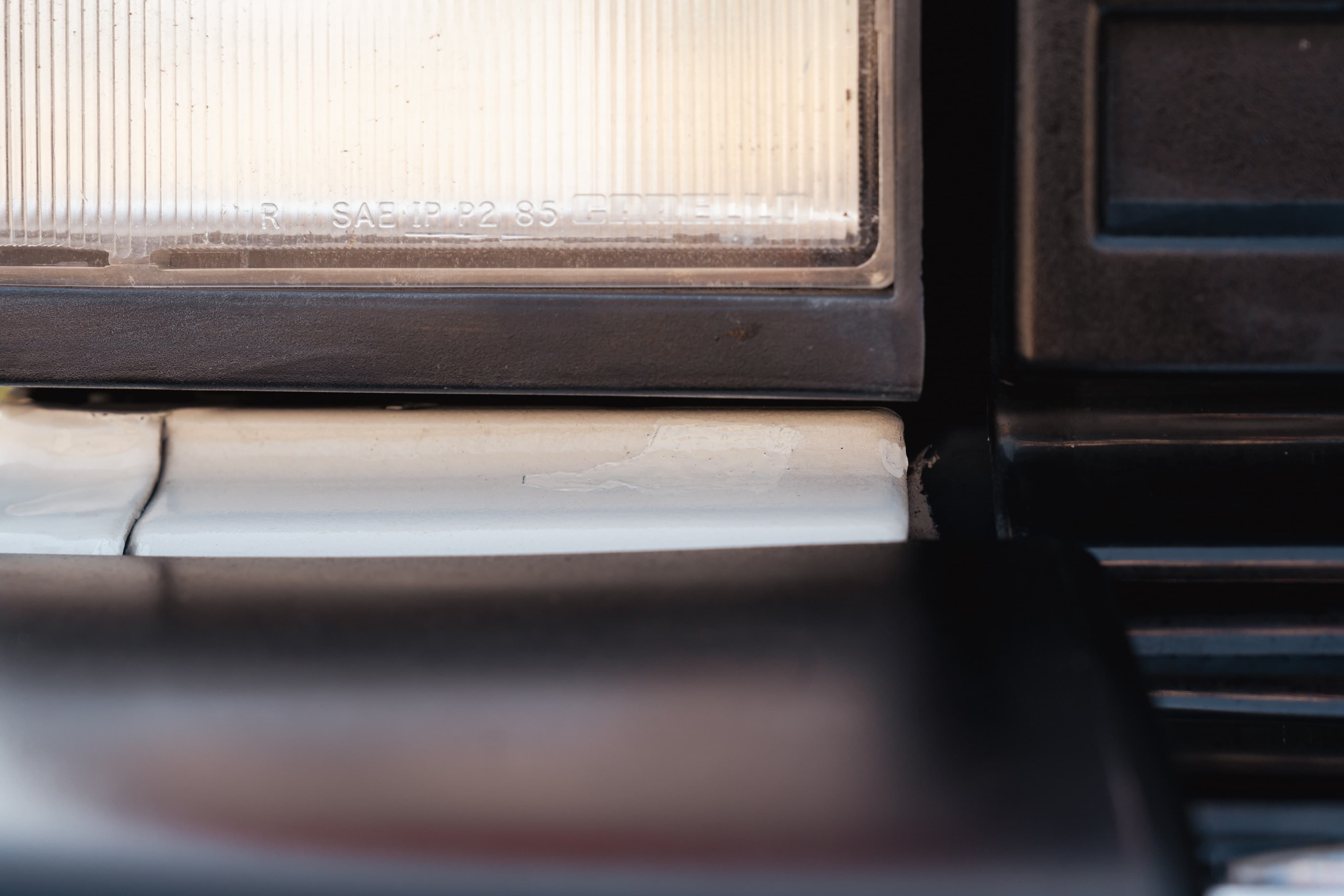 Close-up of a white 1995 Land Rover Range Rover County's headlight trim and dark bumper trim.
