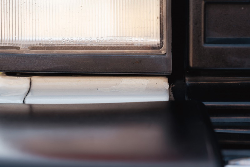Close-up of a white 1995 Land Rover Range Rover County's headlight trim and dark bumper trim.