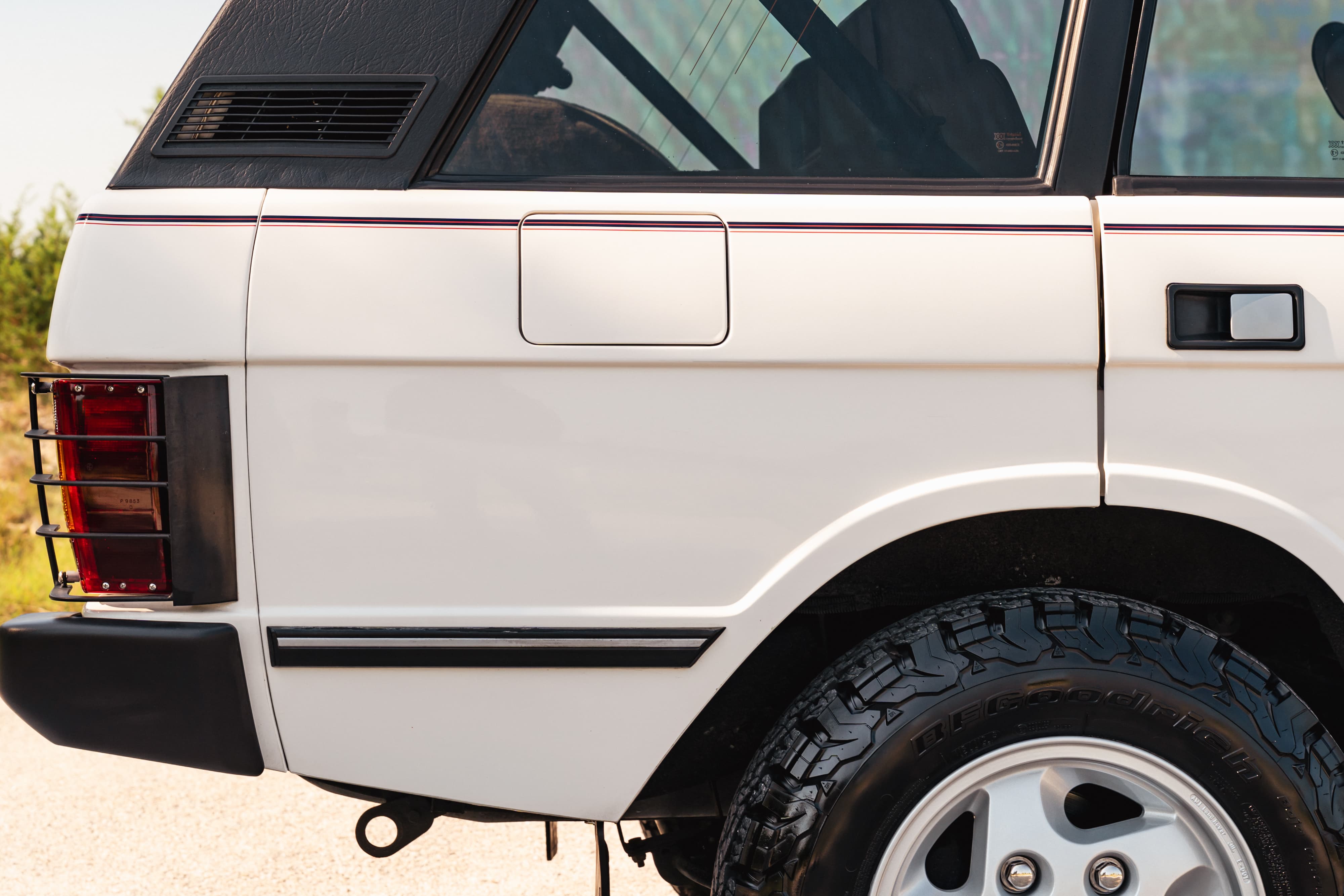 Rear quarter panel of a white 1995 Range Rover County, showing chrome trim, black accents, and alloy rims.