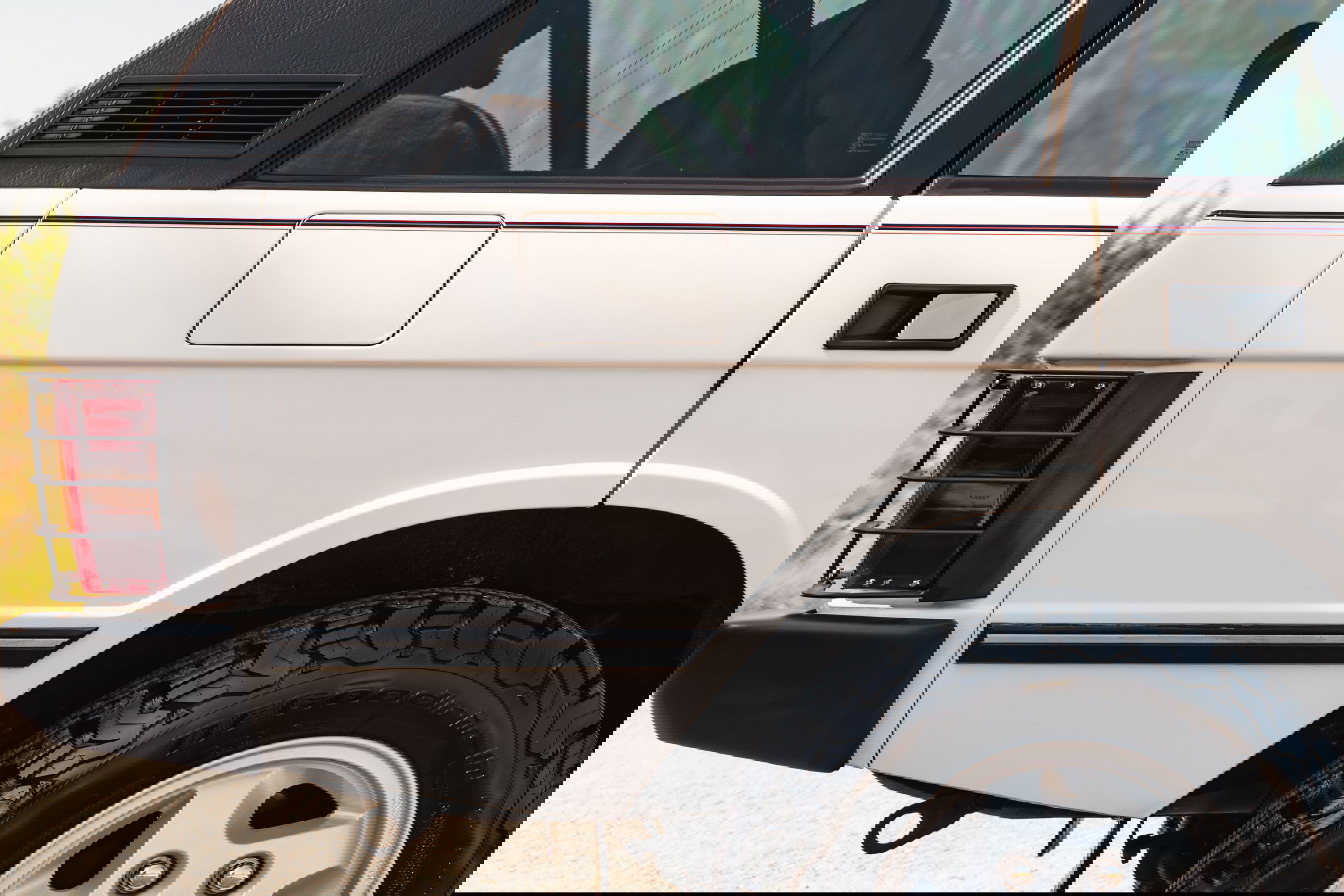 Rear quarter panel of a white 1995 Range Rover County, showing chrome trim, black accents, and alloy rims.