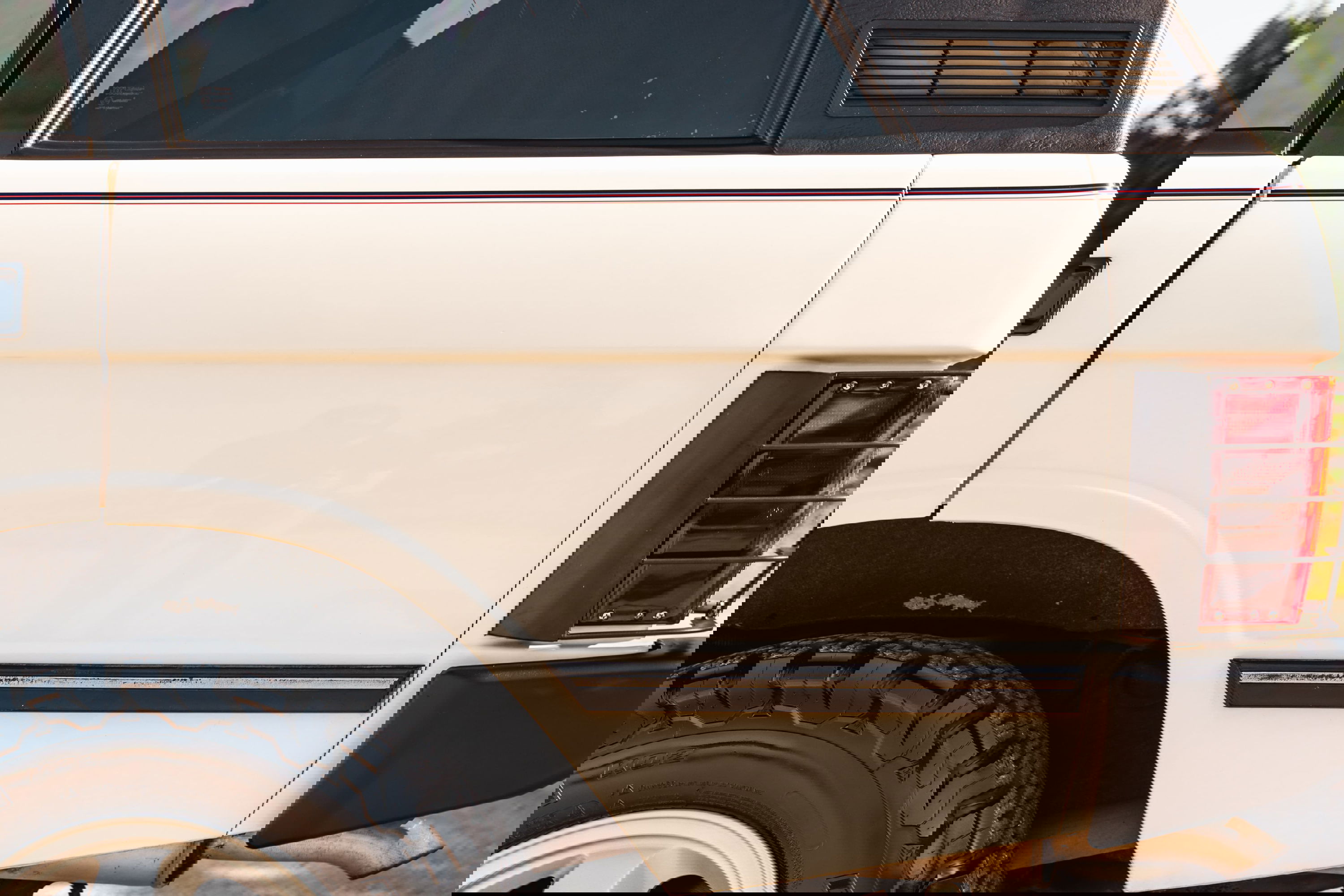 Close-up on the rear quarter panel of a white 1995 Land Rover Range Rover County. Features include a black vinyl roof, red taillight assembly, and off-road tires.