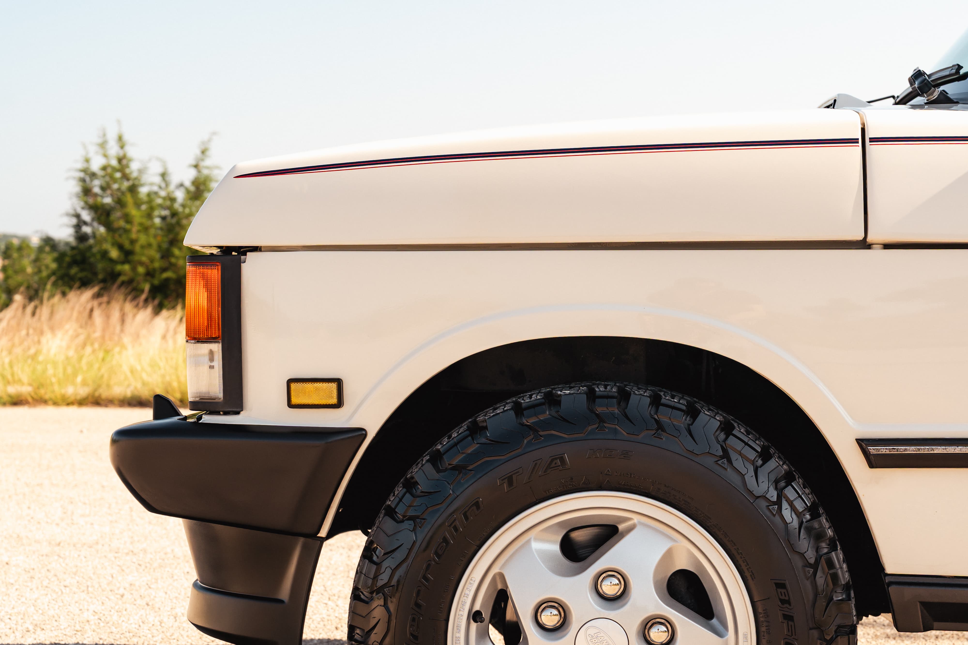 Close up of a white 1995 Range Rover County's front fender, wheel, and bumper.