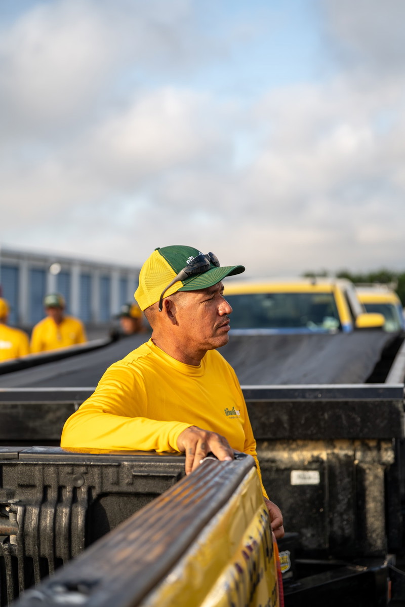 Yellow Grounds Guys Ford F-150 truck, pickup bed, crew cab, with worker in foreground.