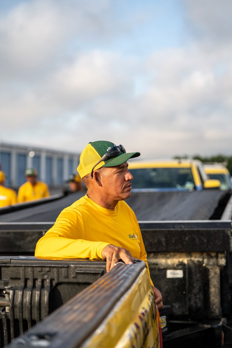 Yellow Grounds Guys Ford F-150 truck, pickup bed, crew cab, with worker in foreground.