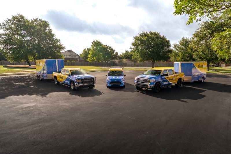 Blue and yellow pickup trucks and a blue car, all with custom livery, parked on asphalt with trailers.