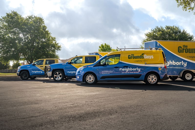 Blue and yellow van with "The Grounds Guys" livery and silver rims.