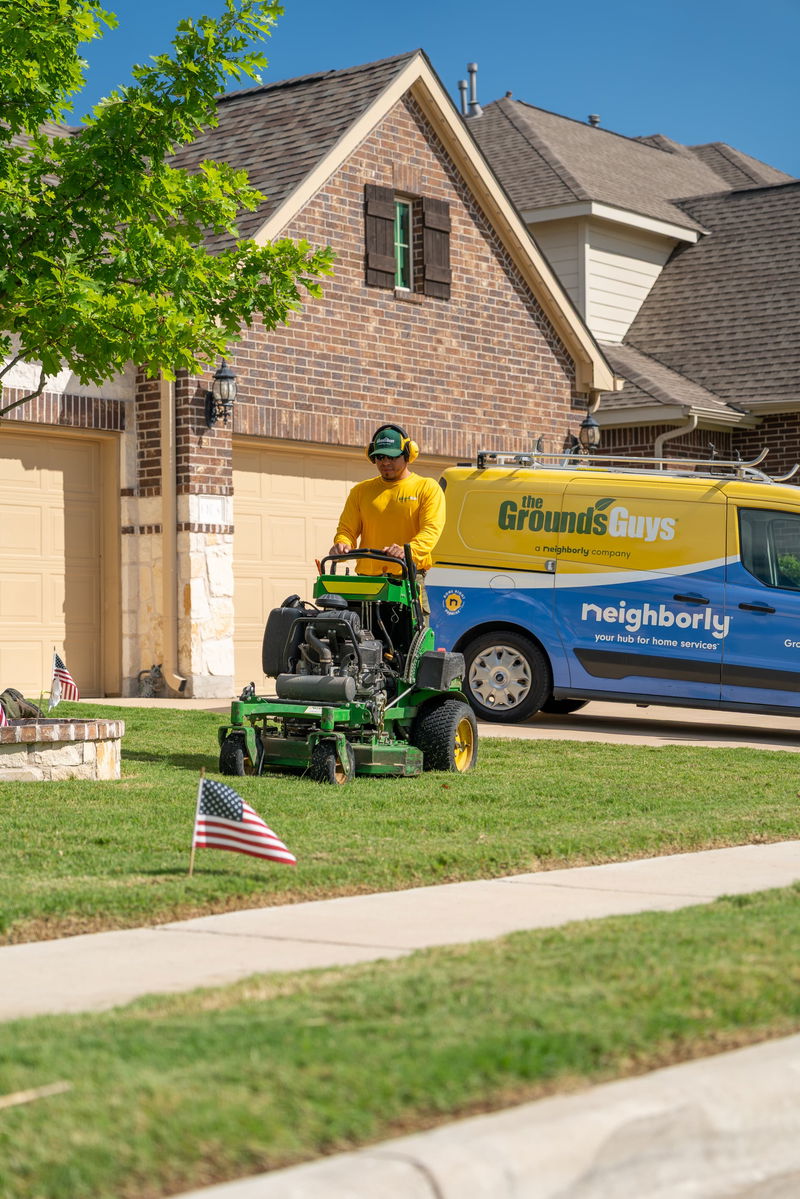 Yellow and blue Neighborly van with "The Ground's Guys" livery, parked beside a lawnmower.
