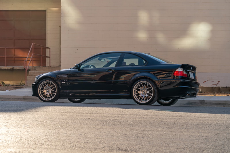 Black 2002 BMW M3 coupe with aftermarket multi-spoke rims and a rear spoiler.
