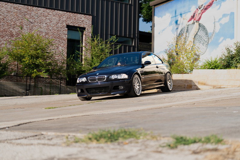 Black 2002 BMW M3 with silver alloy rims parked near a mural.