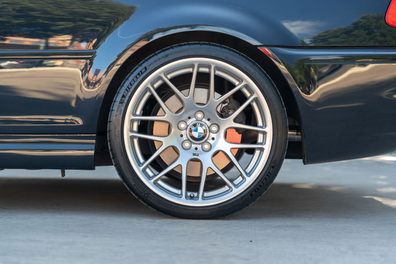 Close-up of a carbon black 2002 BMW M3 rear wheel with silver alloy rims and orange brake calipers.