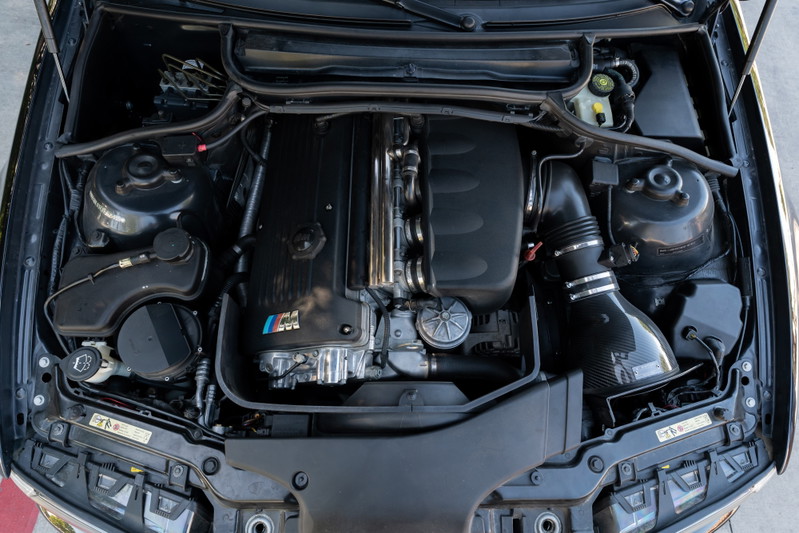 BMW M3 engine bay with carbon fiber intake and M tri-color badge.