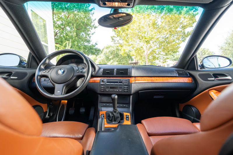 BMW M3 interior with orange leather seats, wood trim, and manual shifter.