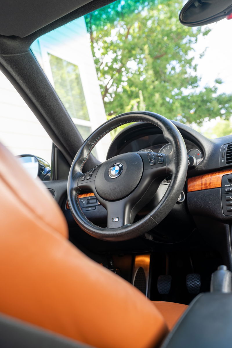 Interior view of a 2002 BMW M3 in Carbon Black, featuring tan leather seats and wood trim.