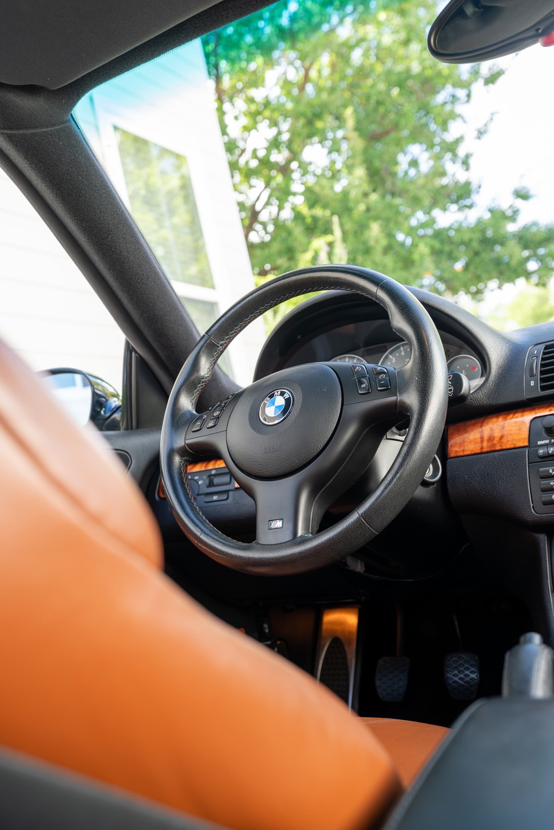 Interior view of a 2002 BMW M3 in Carbon Black, featuring tan leather seats and wood trim.