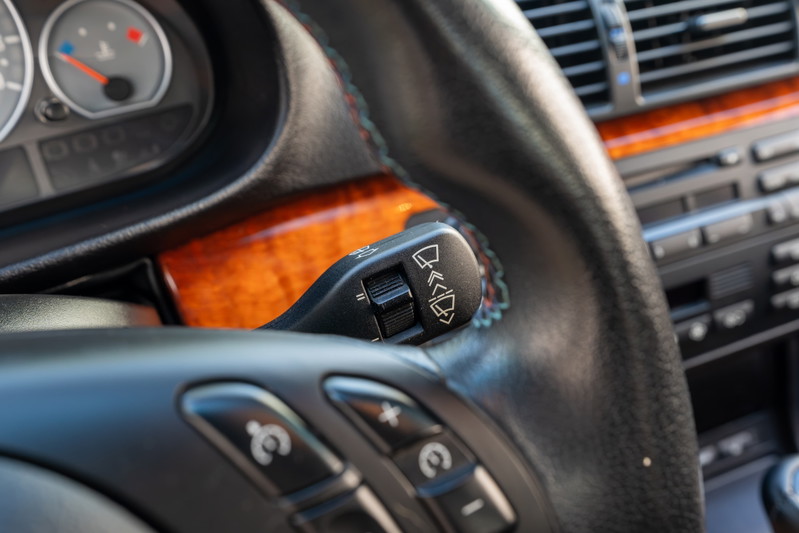Interior shot of a 2002 BMW M3 with wood trim, showing steering wheel controls and wiper stalk.