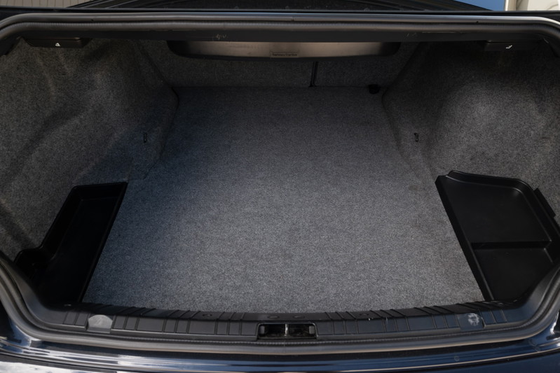 Interior shot of the trunk of a Carbon Black 2002 BMW M3, featuring grey carpeting and black trim.