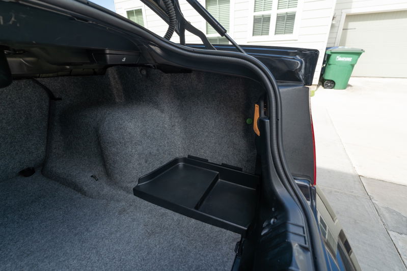 Trunk of a black 2002 BMW M3 with carpeted interior and a removable tray.
