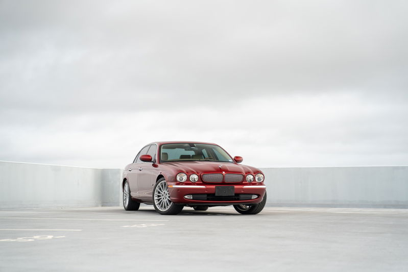 A red 2006 Jaguar XJR sedan with chrome rims and trim sits on a concrete surface.