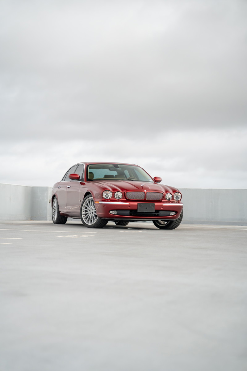 2006 Jaguar XJR in Radiance Red with chrome rims and trim, front three-quarter view.