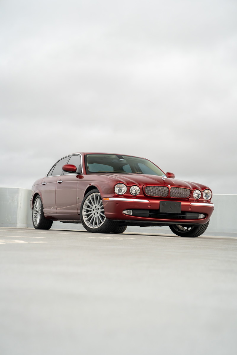 A red 2006 Jaguar XJR sedan with silver multi-spoke rims and chrome trim.