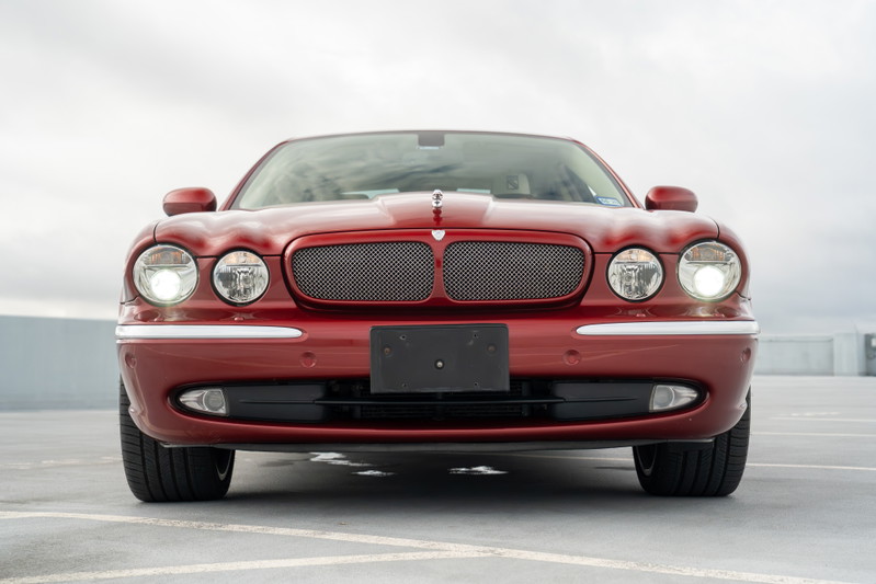 Front view of a red 2006 Jaguar XJR sedan, featuring chrome trim, a mesh grille, and dual headlights.