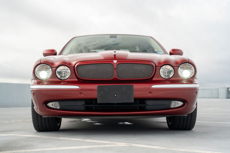 Front view of a red 2006 Jaguar XJR sedan, featuring chrome trim, a mesh grille, and dual headlights.