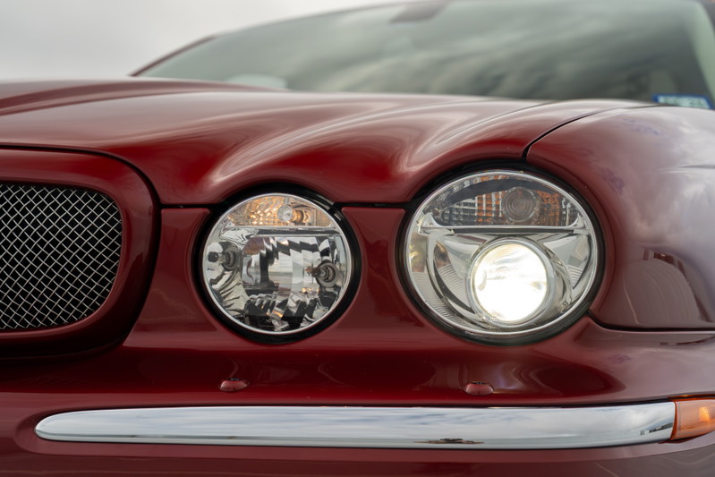 Close-up of a red 2006 Jaguar XJR's dual round headlights and chrome grille.