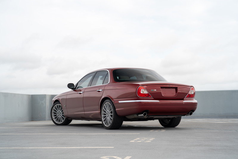 Rear view of a ruby red 2006 Jaguar XJR sedan with multi-spoke alloy rims.