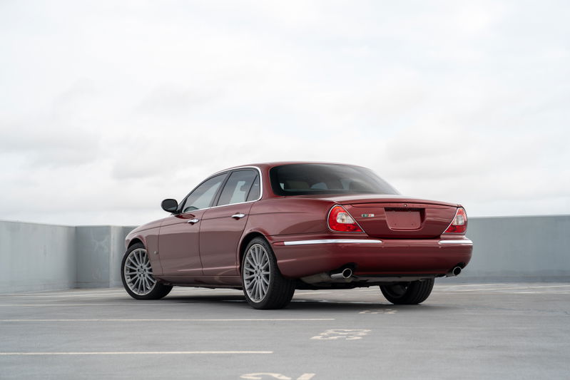 Rear view of a ruby red 2006 Jaguar XJR sedan with multi-spoke alloy rims.