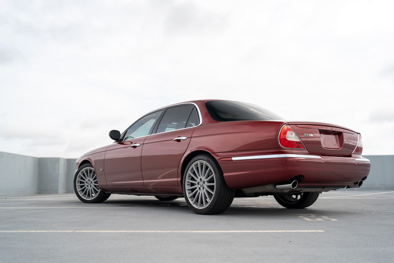 Rear 3/4 view of a red 2006 Jaguar XJR sedan, with chrome trim and silver alloy rims.