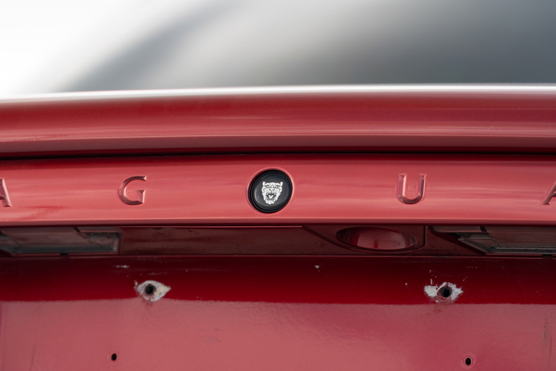 Close-up of red 2006 Jaguar XJR rear trim with chrome lettering and jaguar emblem.