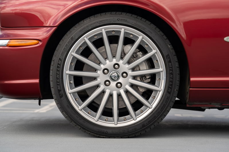 Close-up of a red 2006 Jaguar XJR with silver multi-spoke alloy rims and Michelin tires.
