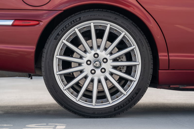 Radiance Red 2006 Jaguar XJR rear wheel with silver multi-spoke rims and Michelin Pilot Sport tires.