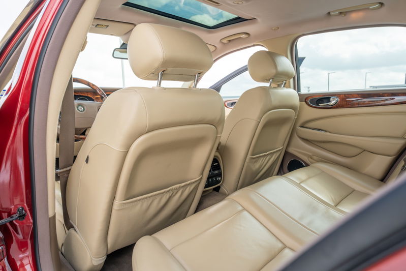 Interior of a 2006 Jaguar XJR in radiance red, featuring beige leather seats, wood trim, and sunroof.
