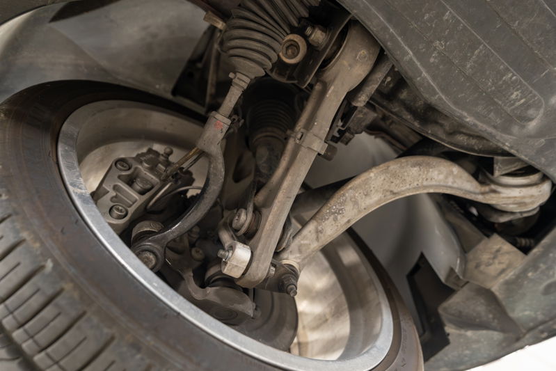 Close-up of 2006 Jaguar XJR's front suspension components, showing aluminum control arms and brake caliper.