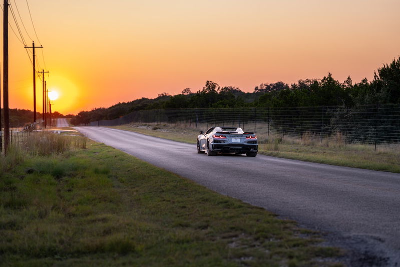 2025 Chevrolet Corvette Z06 convertible in Sea Wolf Gray, driving on a rural road at sunset.