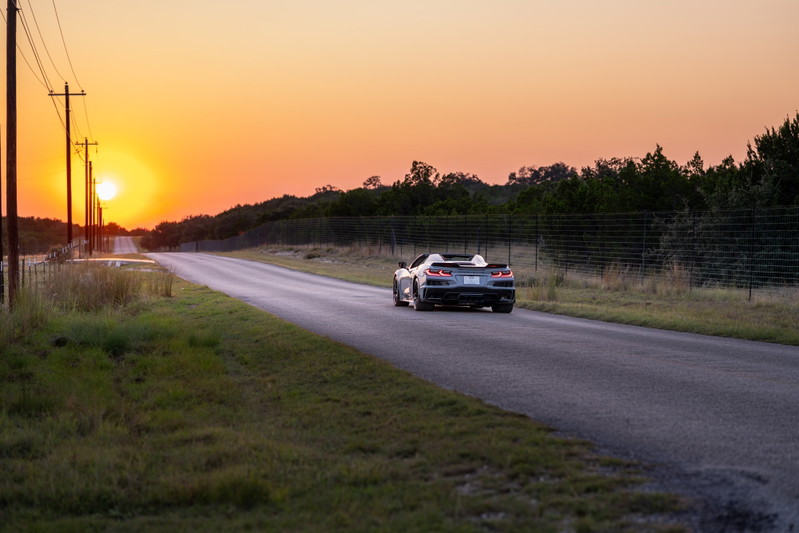 2025 Chevrolet Corvette Z06 convertible in Sea Wolf Gray, driving on a rural road at sunset.