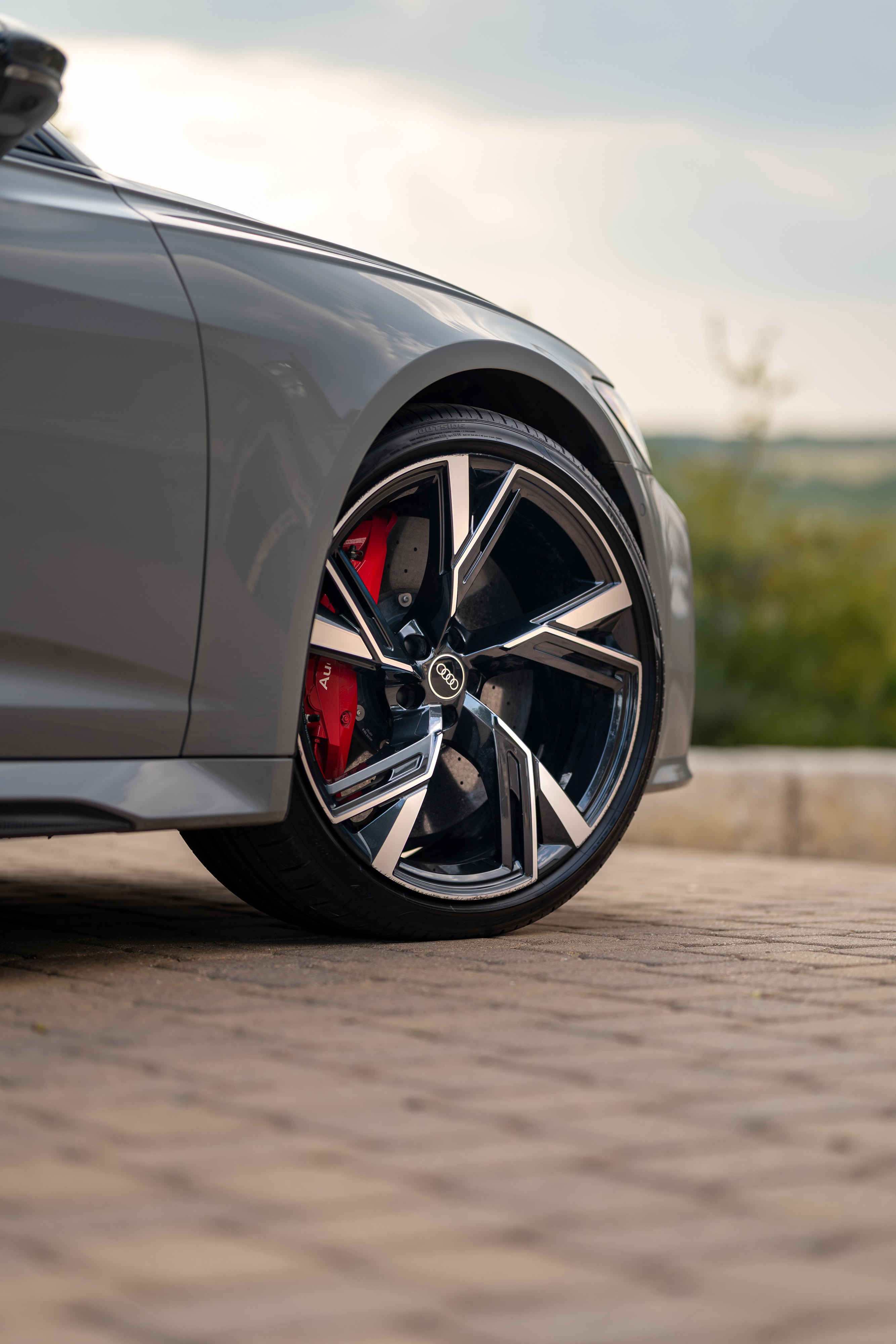 Close-up of a Nardo Grey 2022 Audi RS6 Avant's front wheel, featuring black and silver multi-spoke rims and red brake calipers.