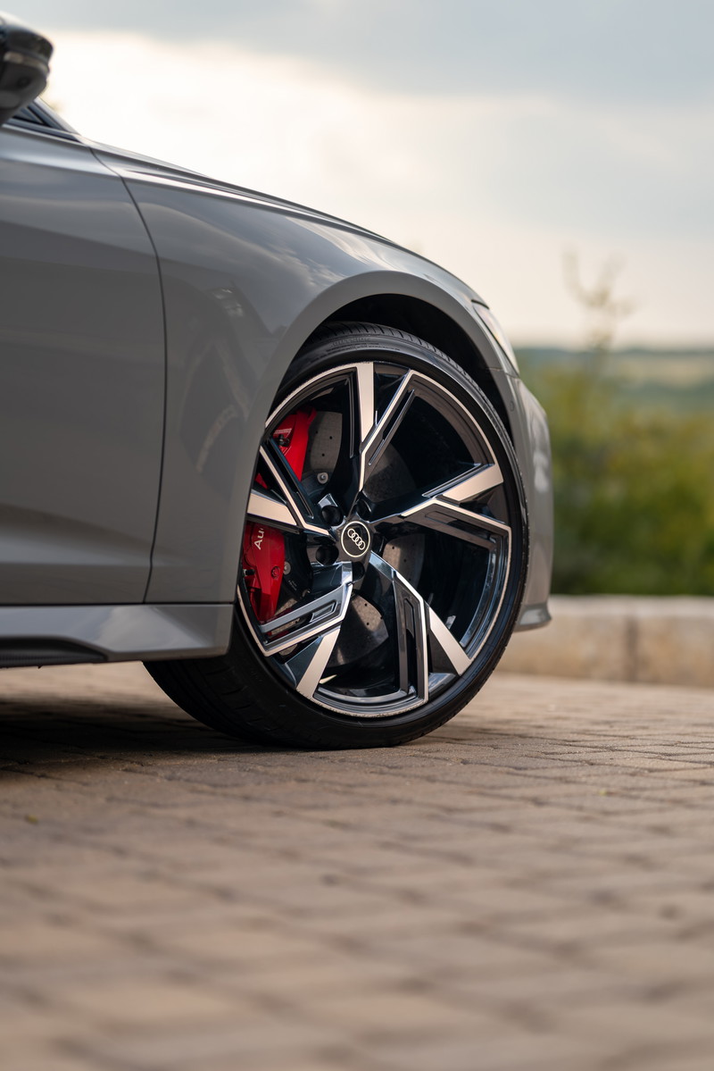 Close-up of a Nardo Grey 2022 Audi RS6 Avant's front wheel, featuring black and silver multi-spoke rims and red brake calipers.