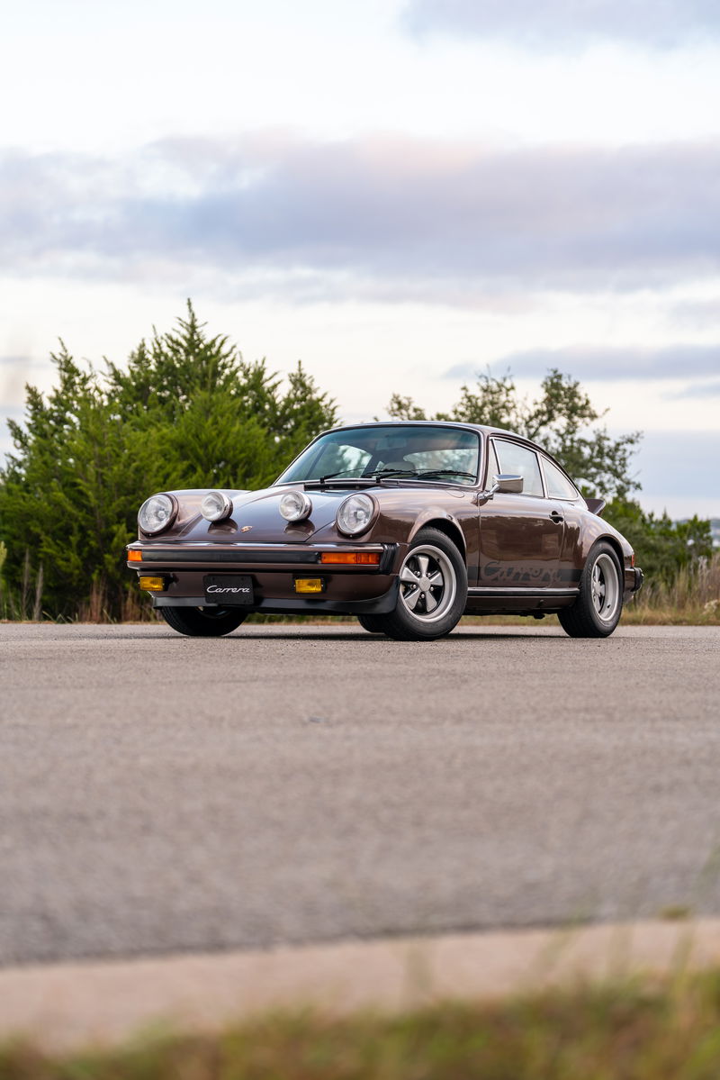 Brown metallic 1975 Porsche 911 Carrera with Fuchs rims and black Carrera livery.