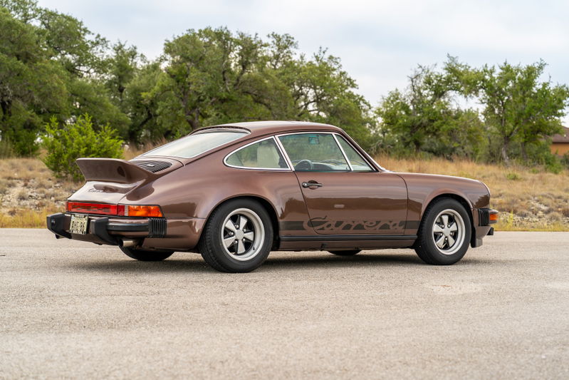 A brown 1975 Porsche 911 Carrera with a ducktail spoiler and Fuchs rims.